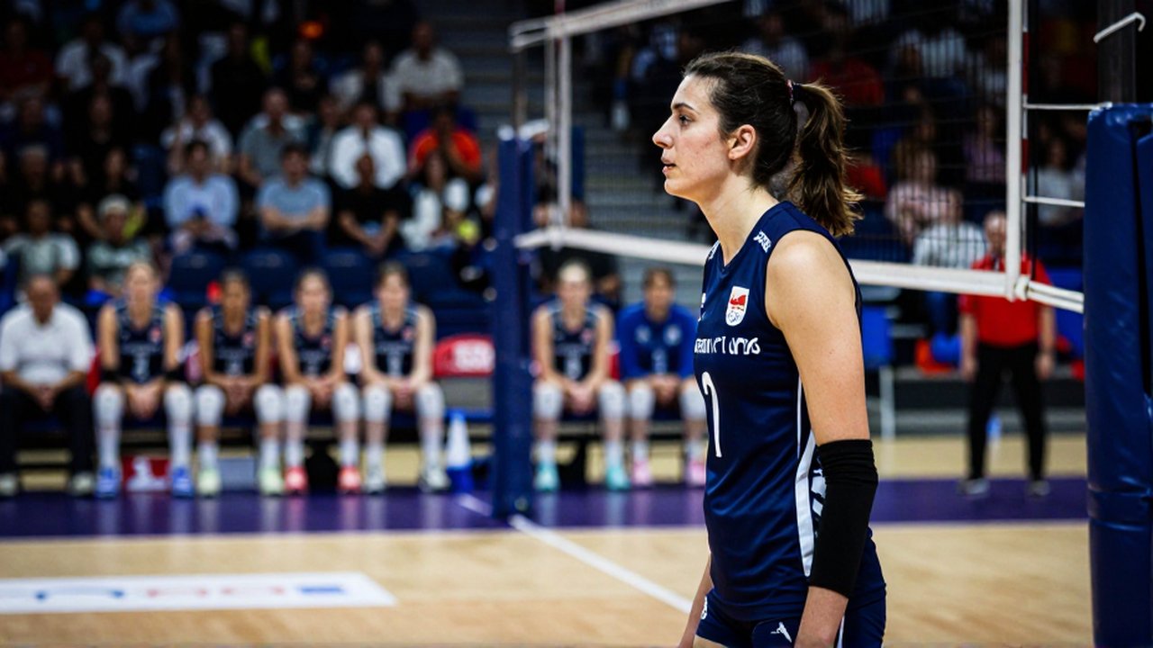 A professional female volleyball player in a navy jersey looks toward her coach on the court.