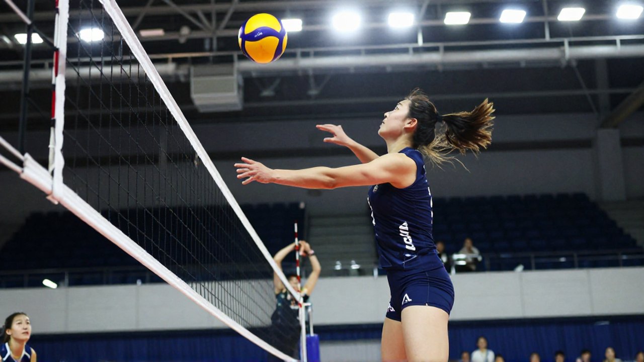 A female volleyball player leaps mid-air to spike the ball over a net in a bright arena.