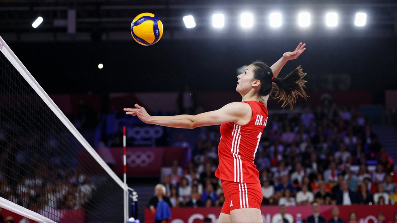 A female volleyball player in a red and white uniform leaps to spike a ball at a net.