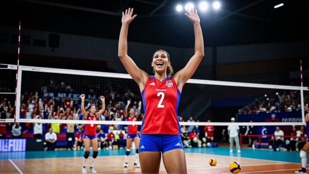 A female volleyball player in a red and blue uniform celebrates a point on an indoor court.